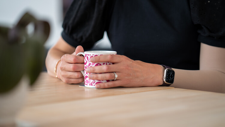 A photo of a person's torso holding a mug that is resting on a table.
